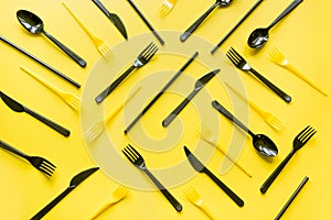 Disposable picnic black knife and forks in diagonal on yellow. Top view. Flat lay