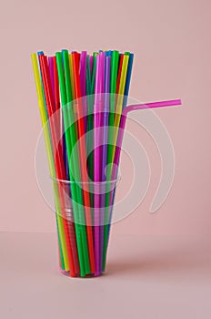 disposable plastic colored straws in a plastic cup on a pink background