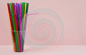 disposable plastic colored straws in a plastic cup on a pink background