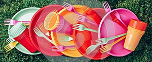 Disposable plastic tableware - plates, forks, spoons. Colored plastic disposable tableware on green grass moss