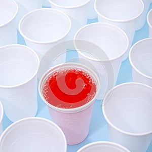 Disposable plastic white empty cups on and one glass filled with red lemonade