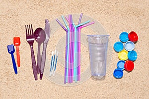 Disposable single use plastic objects that cause pollution of the environment, especially oceans. Top view on sand