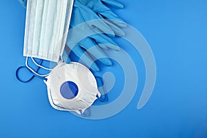 Disposable surgical face masks, white respirator and rubber gloves on blue background