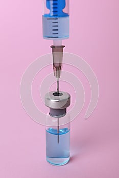 Disposable syringe with needle and vial on pink background, closeup