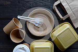 Disposable takeaway food boxes and tableware on dark wooden background. Nature friendly kitchen utensil