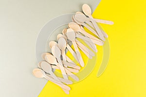 Disposable wooden spoons, forks, picnic and fast food knives are scattered on a colored background.