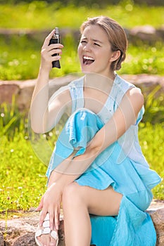 Dissapointed and Angry Young Caucasian Woman Shouting at Her Cellphone. Sitting on the Ground Against Green Grass photo