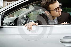 Dissapointed young man is peeking from the window. He is looking at something behind his car photo