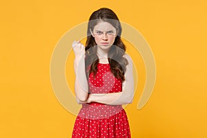 Dissatisfied angry strict young brunette woman girl in red summer dress posing isolated on yellow background studio