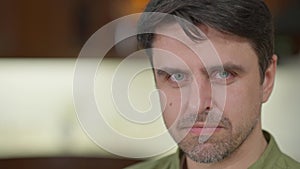 Dissatisfied Caucasian man looking at camera with angry facial expression posing indoors on the right. Close-up of angry