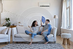 Dissatisfied couple sit on sofa with fan and remote controller