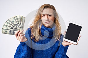 Dissatisfied curly blonde woman with tablet and money in hand