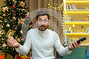 Dissatisfied and disappointed man looking at camera nervously trying to do online shopping while sitting for christmas