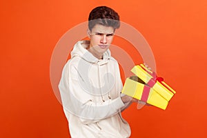 Dissatisfied frustrated teenager in casual hoodie holding open gift box, upset with bad present, unjustified expectations