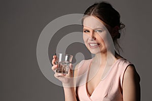 Dissatisfied girl with glass of water. Close up. Gray background
