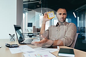 Dissatisfied hispanic man looking at camera and showing clock, businessman frustrated waiting for colleague to be late