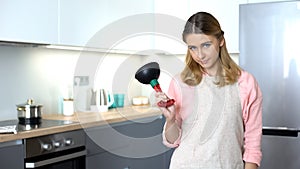 Dissatisfied housekeeper showing plunger, tool to unclog drain, plumber service