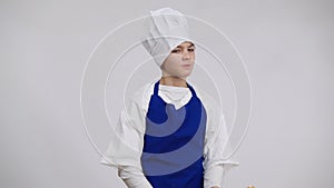 Dissatisfied little chef in uniform threatening with rolling pin posing at white background. Portrait of handsome