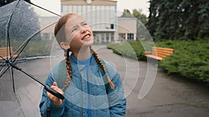 Dissatisfied little girl city street outside bad weather rain schoolgirl with umbrella learner school unhappy child kid