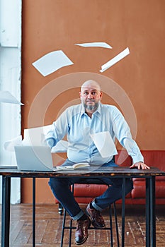 Dissatisfied mature businessman at office desk throwing paper documents in air