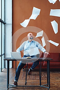 Dissatisfied mature businessman at office desk throwing paper documents in air