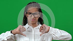 Dissatisfied nerd African American teen girl showing thumbs down on green screen looking at camera. Portrait of