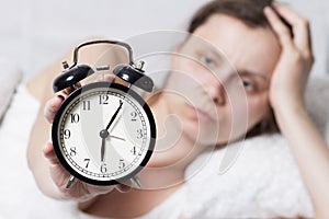 Dissatisfied sleepy woman holding a ringing alarm clock at 6 am.