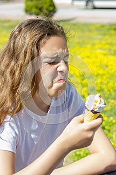 Dissatisfied unhappy teen girl eats tasteless ice cream in a waffle cone in summer. Selective focus