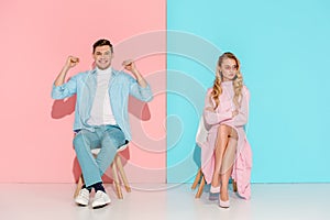 dissatisfied woman with arms crossed and cheering man with clenched fists sitting on chairs