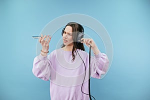 Dissatisfied woman in sweatshirt connects wired headphones to smartphone with cable with evil face on blue background