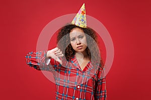 Dissatisfied young african american girl in pajamas homewear, birthday hat posing resting at home isolated on red