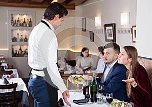 Dissatisfied young couple talking to apologetic waiter