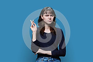 Dissatisfied young female looking at camera on blue background