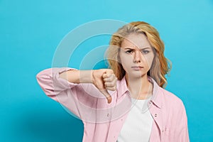 Dissatisfied young woman showing thumb down gesture on light blue background