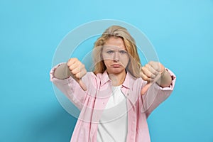 Dissatisfied young woman showing thumbs down on light blue background