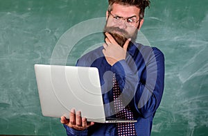 Distance education concept. Hipster teacher wear eyeglasses and necktie holds laptop surfing internet. Teacher bearded