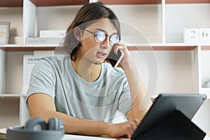 Distance education concept, Teen boy talking on phone and using tablet to lesson class online