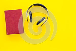 Distance education, e-learning concept. Headphones near hardback book with empty cover on yellow background top view