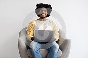 Distance Job. Happy Young Black Freelancer Guy Sitting With Laptop In Armchair