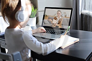 Distance learning. Cheerful little girl girl in headphones using laptop studying through online e-learning system.