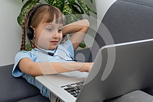 Distance learning. Cheerful little girl girl in headphones using laptop studying through online e-learning system.