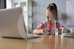 Distance learning. Cheerful little girl girl in headphones using laptop studying through online e-learning system.