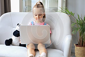 Distance learning. Cheerful little girl using laptop computer studying through online e-learning system.
