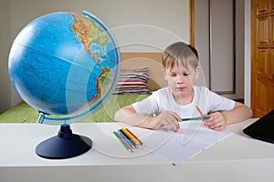 Distance learning, geography lesson. The boy is sitting on the bed with a globe at the laptop