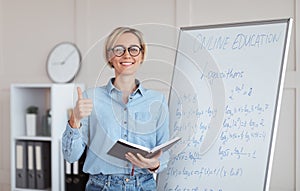 Distance learning. Happy female teacher giving online math class, showing thumb up gesture near blackboard at home