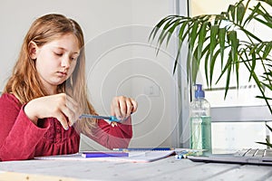 Distance learning online education. Schoolgirl studying at home with a laptop and doing school homework. Sharpen a pencil with a