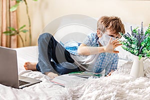 Distance learning online education. Sickness boy in medical mask touching green plant and studying home with laptop