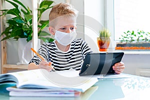 Distance learning online education. Sickness schoolboy in medical mask studying at home with digital tablet in hand and photo