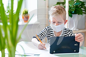 Distance learning online education. Sickness schoolboy in medical mask studying at home with digital tablet in hand and photo