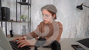 Distance learning. Schoolgirl studying online using laptop. School student wearing headphones watching internet course